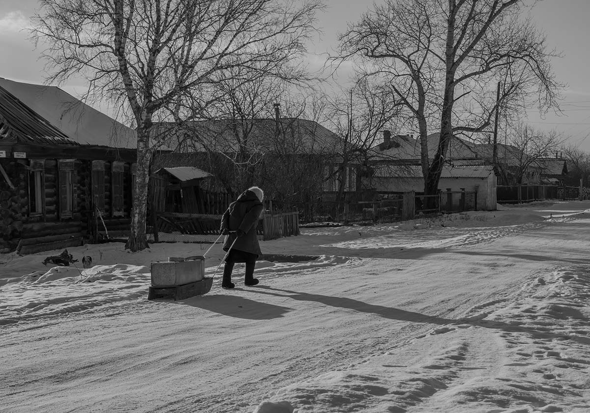 photo "***" tags: street, genre, black&white, snow, деревенская улица, деревня, дома, зима в деревне, санки, санки с грузом, старушка